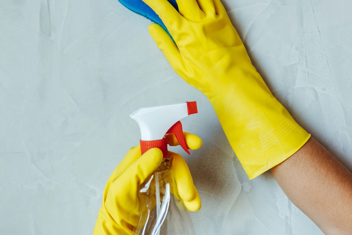 Individual wearing yellow rubber gloves grips a spray bottle, prepared for cleaning tasks.