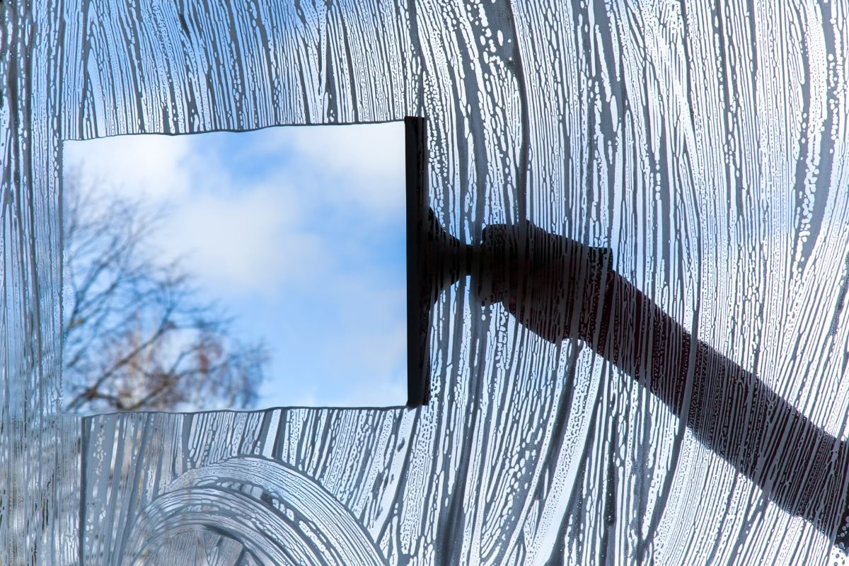 A person holds a mirror up to a window, reflecting the outside view and creating an interplay of light and perspective.